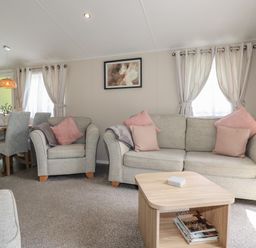 A living room with gray sofas pink cushions a wooden coffee table and a dining table with chairs at Pams Place in Crantock