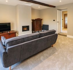A living room with a gray sofa a TV on a wooden chest a built-in fireplace and wooden cabinet at Luham Cottage Edenhall near Langwathby