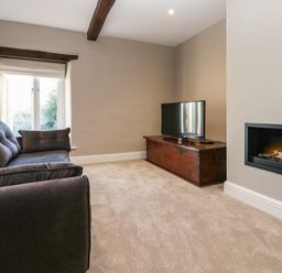 A living room with a dark sofa a television on a wooden chest and a wall-mounted fireplace at Luham Cottage Edenhall near Langwathby
