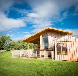A wooden cabin with a fenced porch in a grassy area with trees at Aurae in Cawdor near Inverness