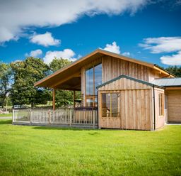 A wooden house with large windows and a fenced porch on a grassy lawn at Atlas in Cawdor near Inverness