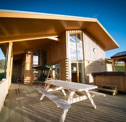 A wooden deck with a picnic table swing and hot tub outside a wooden house at Atlas in Cawdor near Inverness
