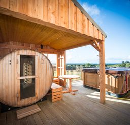 A wooden sauna, a round table with benches, and a covered hot tub on a wooden deck at Atlas in Cawdor near Inverness