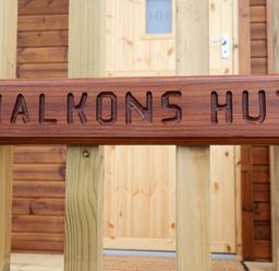 A wooden sign reading Halkons Hut attached to vertical wooden beams with a wooden door in the background at Shepherds Hut in Garthorpe near Scunthorpe