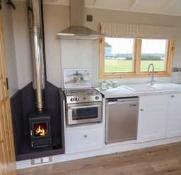 A kitchen with a wood stove cooker sink dishwasher and window at Shepherds Hut in Garthorpe near Scunthorpe