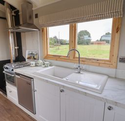 A kitchen with a sink under a window and a stove next to a refrigerator at Shepherds Hut in Garthorpe near Scunthorpe