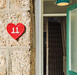 A stone wall with a red heart-shaped house number 11 and an open door showing a hallway with stairs at 11 Belgravia Street in Penzance