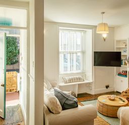 A living room with a beige sofa a round wooden coffee table a wall mounted TV and a stone fireplace at 11 Belgravia Street in Penzance