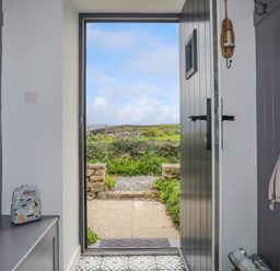 A doorway view from inside showing an open black door leading to a garden path at Bwthyn Y Swnt in Moelfre