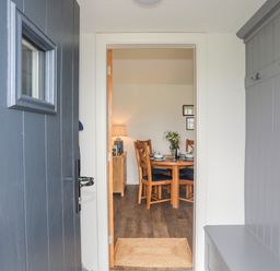 Entryway with a blue door and gray bench with hooks leading to a dining area with a wooden table and chairs at Bwthyn Y Swnt in Moelfre