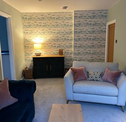 A living room with two sofas a wooden coffee table a lamp on a cabinet and patterned wallpaper at Secret Garden 34C Clarence Street Dartmouth