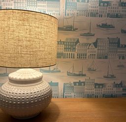 A table lamp with a textured base on a wooden surface and wallpaper with ships and buildings in the background at Secret Garden 34C Clarence Street Dartmouth