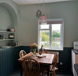 A dining area with wooden table and chairs flowers and wine on table near window with shelves on wall at Secret Garden 34C Clarence Street Dartmouth