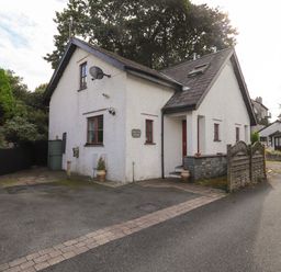 White cottage with satellite dish and small garden area beside a narrow street at Cherry Tree Cottage in Windermere