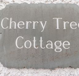 A carved stone sign with the text Cherry Tree Cottage on a textured white wall at Cherry Tree Cottage in Windermere