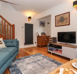 A living room with a blue sofa next to wooden stairs a TV on a cabinet and a table with pastries at Cherry Tree Cottage in Windermere