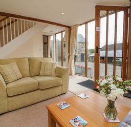 A living room with a beige sofa and coffee table with flowers near glass doors at Hunstone Barn in South Molton