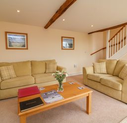 A living room with two beige sofas a wooden coffee table with books and a vase of flowers and stairs in the background at Hunstone Barn South Molton