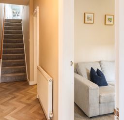 A hallway with carpeted stairs and a radiator next to a room with a striped sofa and two framed pictures on the wall at Bay Tree Cottage Keswick
