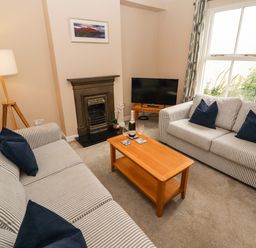 A living room with two striped sofas and a wooden coffee table with a bottle and glasses at Bay Tree Cottage in Keswick
