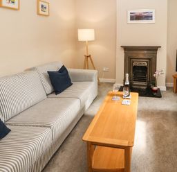 A living room with striped sofas a wooden coffee table with drinks a fireplace and a television at Bay Tree Cottage Keswick