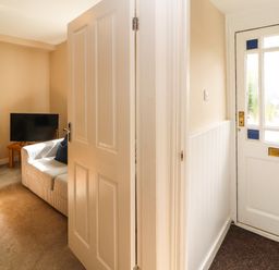 A hallway with a white door leading to a living room with a sofa a television and a wooden table at Bay Tree Cottage in Keswick