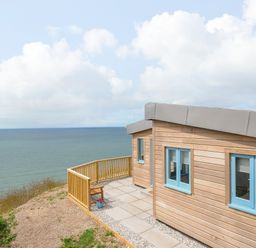 A wooden cabin with blue windows next to a patio overlooking the sea at Solana in Whitsand Bay