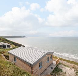 A wooden cabin on a hillside overlooking the ocean with another cabin in the distance at Solana in Whitsand Bay
