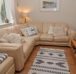 A living room with a beige corner sofa, cushions, a patterned rug, a side table with a lamp, and a wooden coffee table at Alberts Den in Falmouth