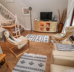 A living room with wooden chairs a wooden dining table a television on a wooden cabinet and rugs on the floor at Alberts Den in Falmouth