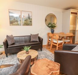 A living room with brown leather sofa and chairs a wooden coffee table a dining table with chairs and a kitchen in the background at Reubens Cottage in Fremington Devon