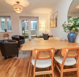 A dining and living area with wooden table and chairs leather armchairs and a glass door at Reubens Cottage in Fremington Devon