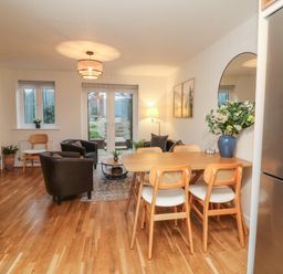 A dining area with wooden table and chairs next to a living room with armchairs and a sofa at Reubens Cottage in Fremington Devon