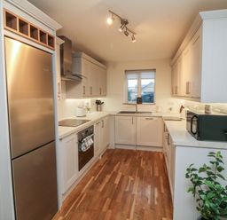 A kitchen with wooden floor cabinets microwave refrigerator oven a window and plants at Reubens Cottage in Fremington Devon