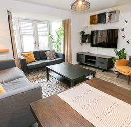 A living room with two gray sofas a yellow armchair a black coffee table a wall-mounted tv and large clock at 20 Bishops Way in Falmouth