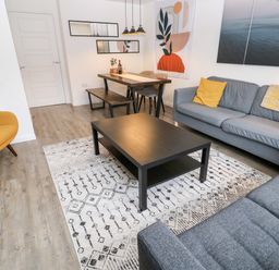 A living room with a coffee table on a patterned rug and a dining table with chairs and a bench at 20 Bishops Way in Falmouth
