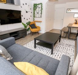 A living room with a large wall clock a yellow armchair and a dining table at 20 Bishops Way in Falmouth