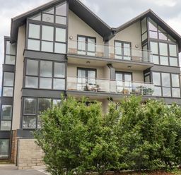 A modern three-story building with large windows and balconies behind green bushes at The Penthouse in Scarborough