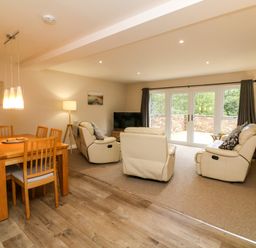A living room and dining area with a wooden dining table and chairs and cream sofas facing a television at Spicery in Tedburn St Mary