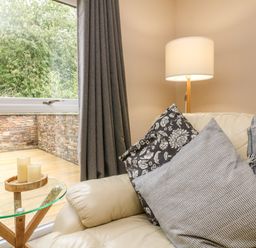 A seating area with cushions and a throw on a sofa next to a lamp and a glass side table with candles at Spicery in Tedburn St Mary