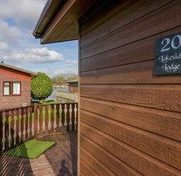 A wooden lodge exterior with a sign reading 20 Lakeside Lodge near wooden railing and a body of water at Lakeside 20 in Warton near Carnforth