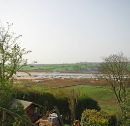 A view of a river with boats and green fields in the background at Riverbank Cottage in Alnmouth