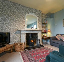A living room with a fireplace a wooden coffee table and a sofa with patterned cushions at Riverbank Cottage in Alnmouth