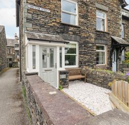 Stone built terraced houses with a small gravel front yard and wooden benches on Compston Street at Woolly End Cottage in Ambleside