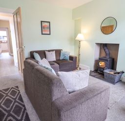 A living room with brown sofas a wood stove and a lamp at Woolly End Cottage in Ambleside