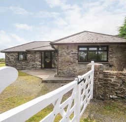 A stone house with a tiled roof and a white gate in front at The Old Forge in Trerulefoot
