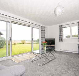 A living room with glass coffee table and sliding doors opening to a garden at The Old Forge in Trerulefoot