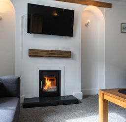 A living room with a fireplace a wall mounted television two sofas and a wooden table at Ayr Farmhouse in St Ives