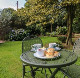 A green metal garden table and chairs with scones jam and cups of tea in a garden at Jasmine Bydown near Barnstaple