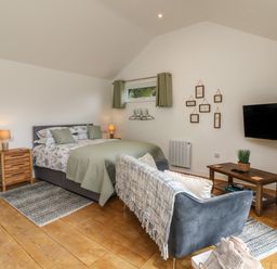 A bedroom with a bed sofa wooden furniture and a wall-mounted TV at Jasmine Bydown near Barnstaple